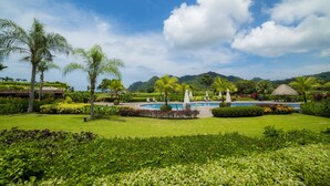 A lush garden with a pool, palm trees, and a mountain backdrop. - Los Suenos Resort Del Mar 3N (Jacó)