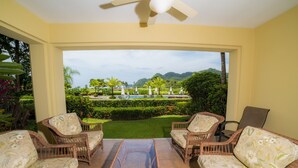 A room with wicker furniture and a glass table, overlooking a pool and garden. - Los Suenos Resort Del Mar 3N (Jacó)