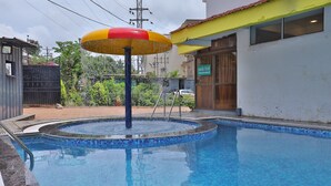 A swimming pool with a water fountain and a colorful umbrella. - Hotel Highland Resort (Mawal)