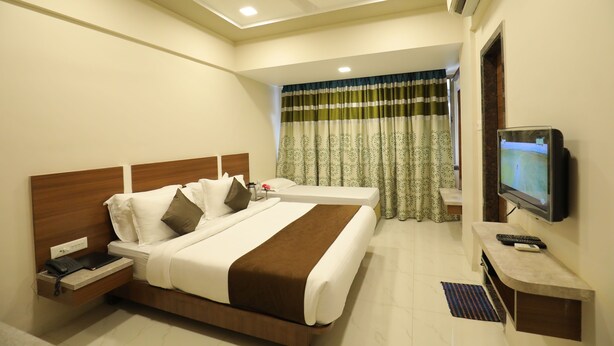 A hotel room with a large bed, a TV, a desk, and a ceiling fan. - Hotel Highland Resort (Mawal)