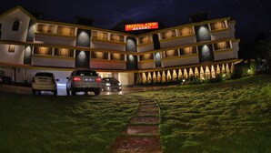 A multi-story hotel with a sign reading "Highland Resort." There are two cars parked in front, and the building has multiple balconies with lights. - Hotel Highland Resort (Mawal)
