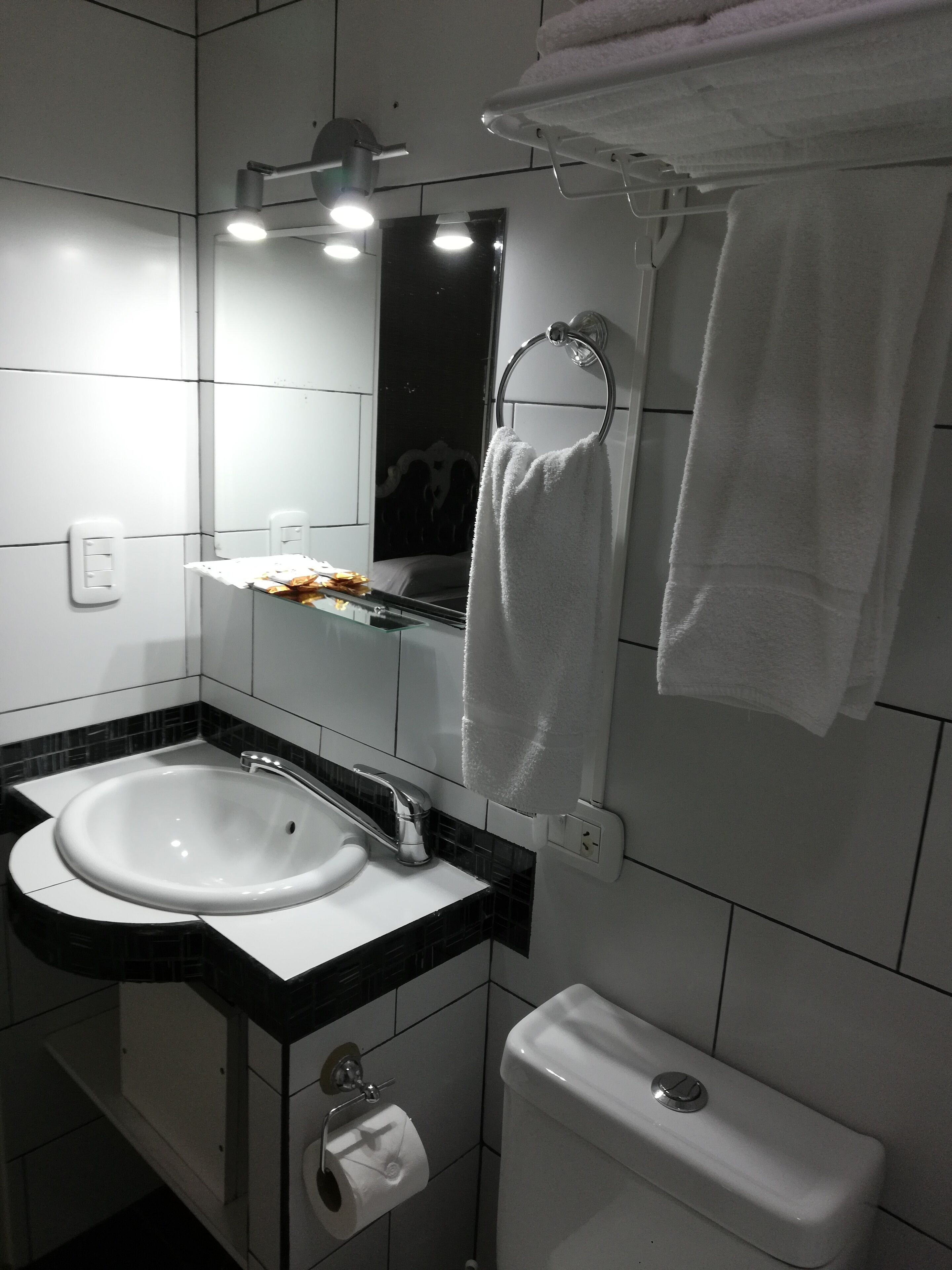 A bathroom with a white sink, mirror, and toilet. There is a towel rack with a towel hanging on it.