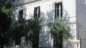 Un edificio blanco con tres ventanas y una puerta, rodeado de árboles.
