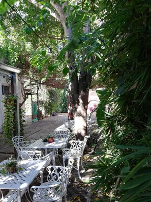 An outdoor seating area with white metal tables and chairs, surrounded by lush greenery and trees. - Casablanca Adrogué (Adrogué)