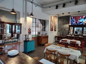 Interior de restaurante con mobiliario de madera, piso a cuadros y una pantalla de televisión mostrando una banda.