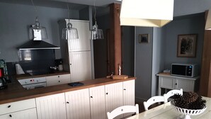 A kitchen with white cabinets, a stove, and a microwave. There is a dining table with chairs and a bowl of pinecones.