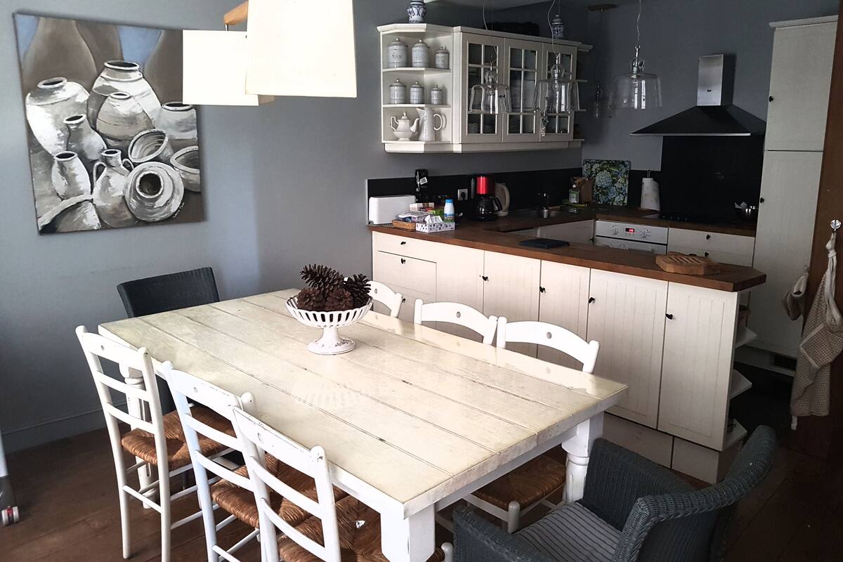 Une cuisine avec des meubles blancs, un plan de travail en bois et un coin repas comprenant une table et des chaises.