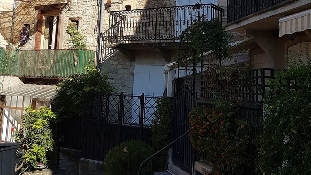 A stone building with a balcony, a street lamp, and a small garden area.