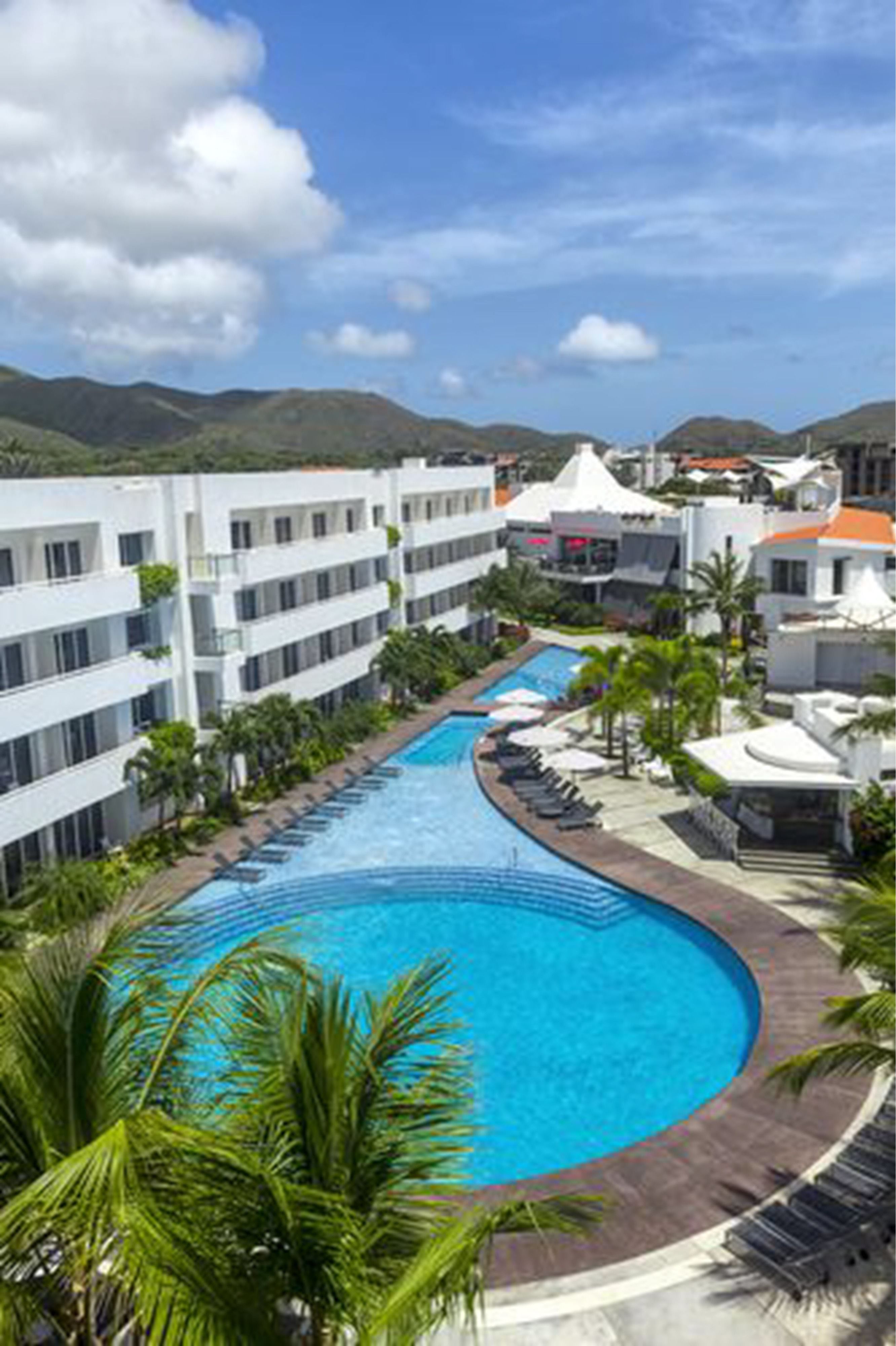 A resort with a large swimming pool, multiple hotel buildings, and palm trees.