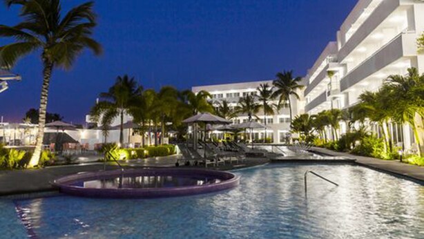 A hotel with a swimming pool, palm trees, and a well-lit outdoor area. - LD Plus (Paraguachí)