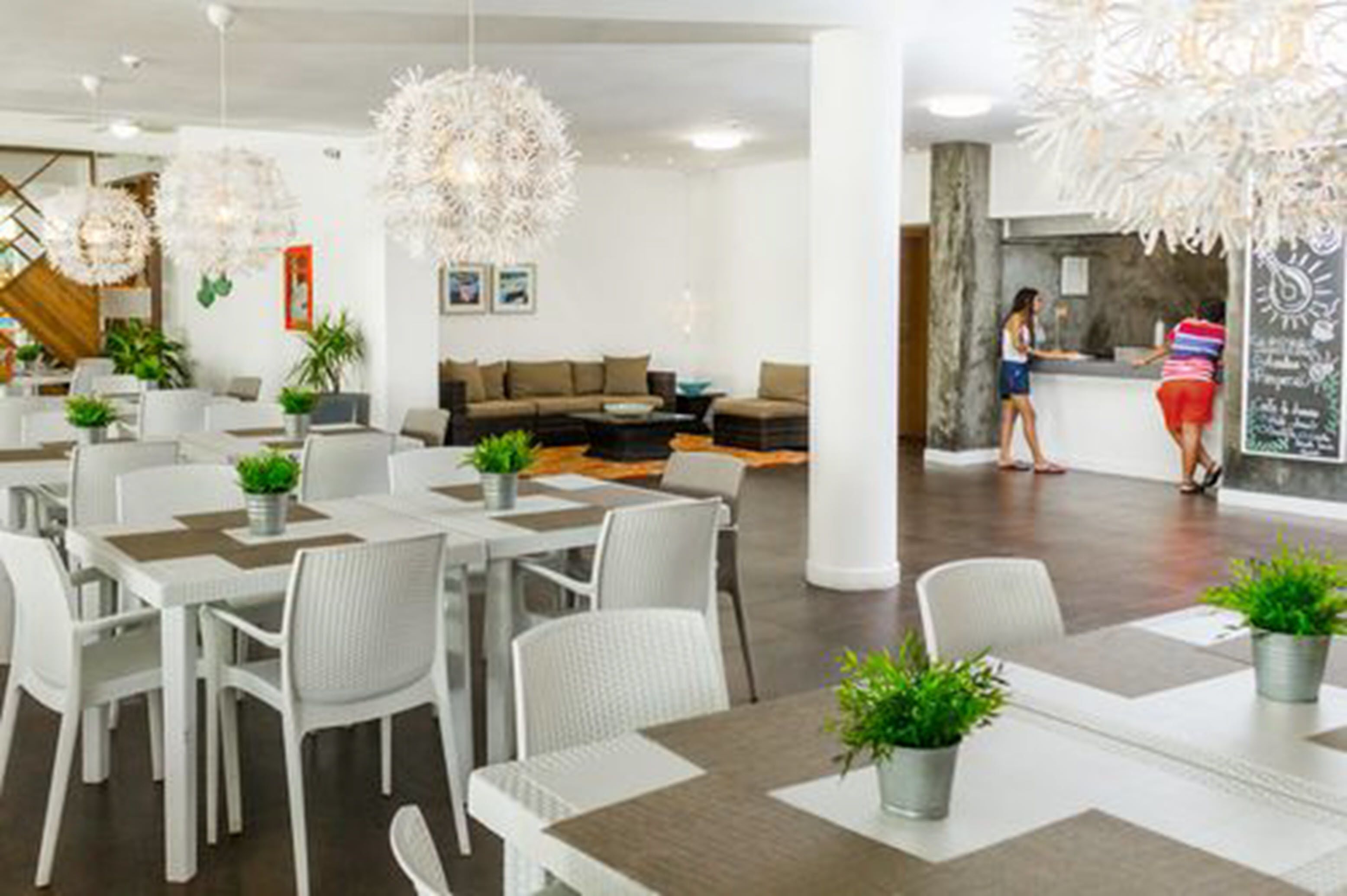 Un moderno vestíbulo de hotel con muebles blancos, una recepción y luminarias decorativas colgantes.