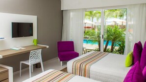 A hotel room with a bed, a desk, a chair, a TV, and a view of a pool and greenery. - LD Plus (Paraguachí)