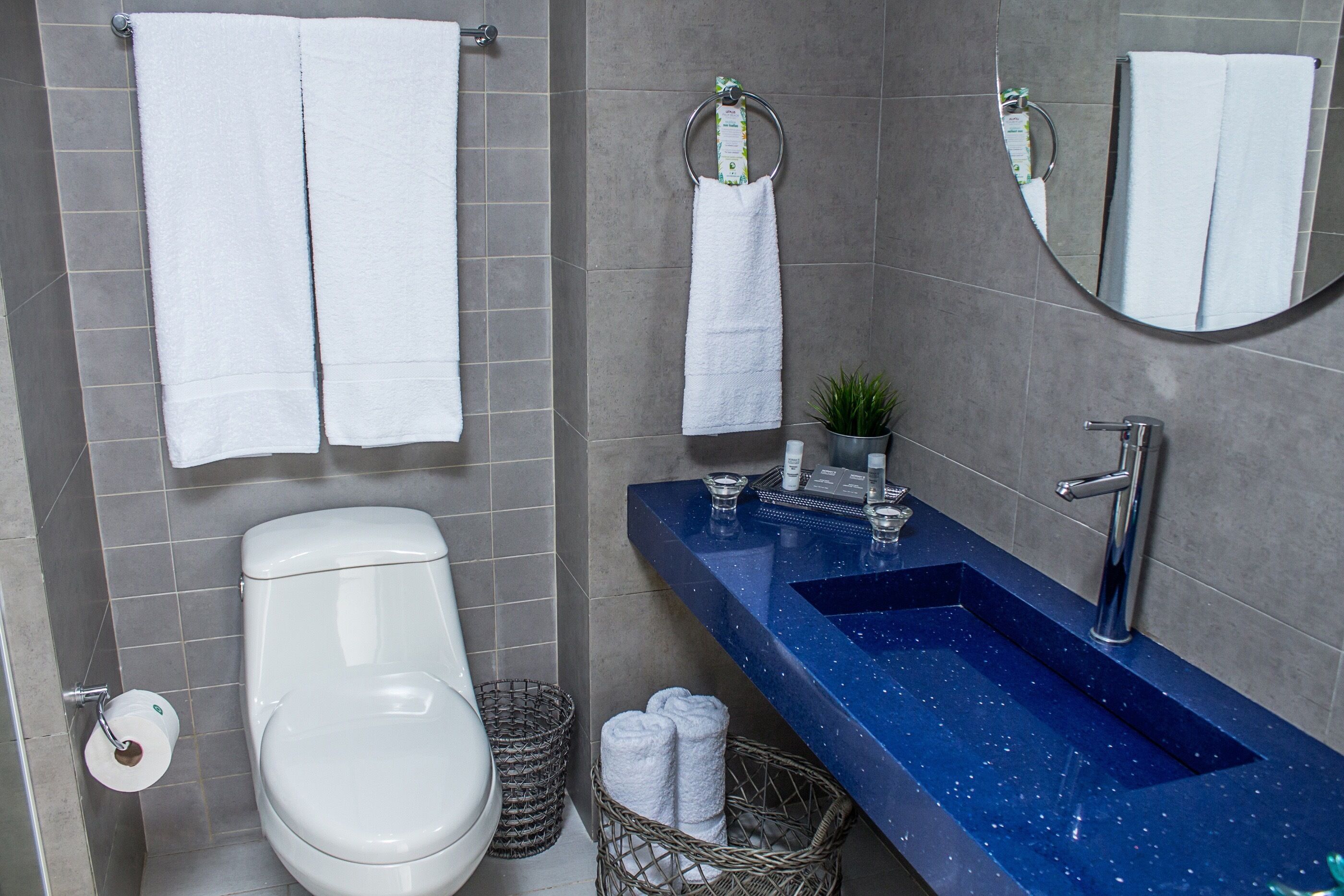 Un bagno con il water bianco, un lavandino blu e due asciugamani bianchi appesi al muro.