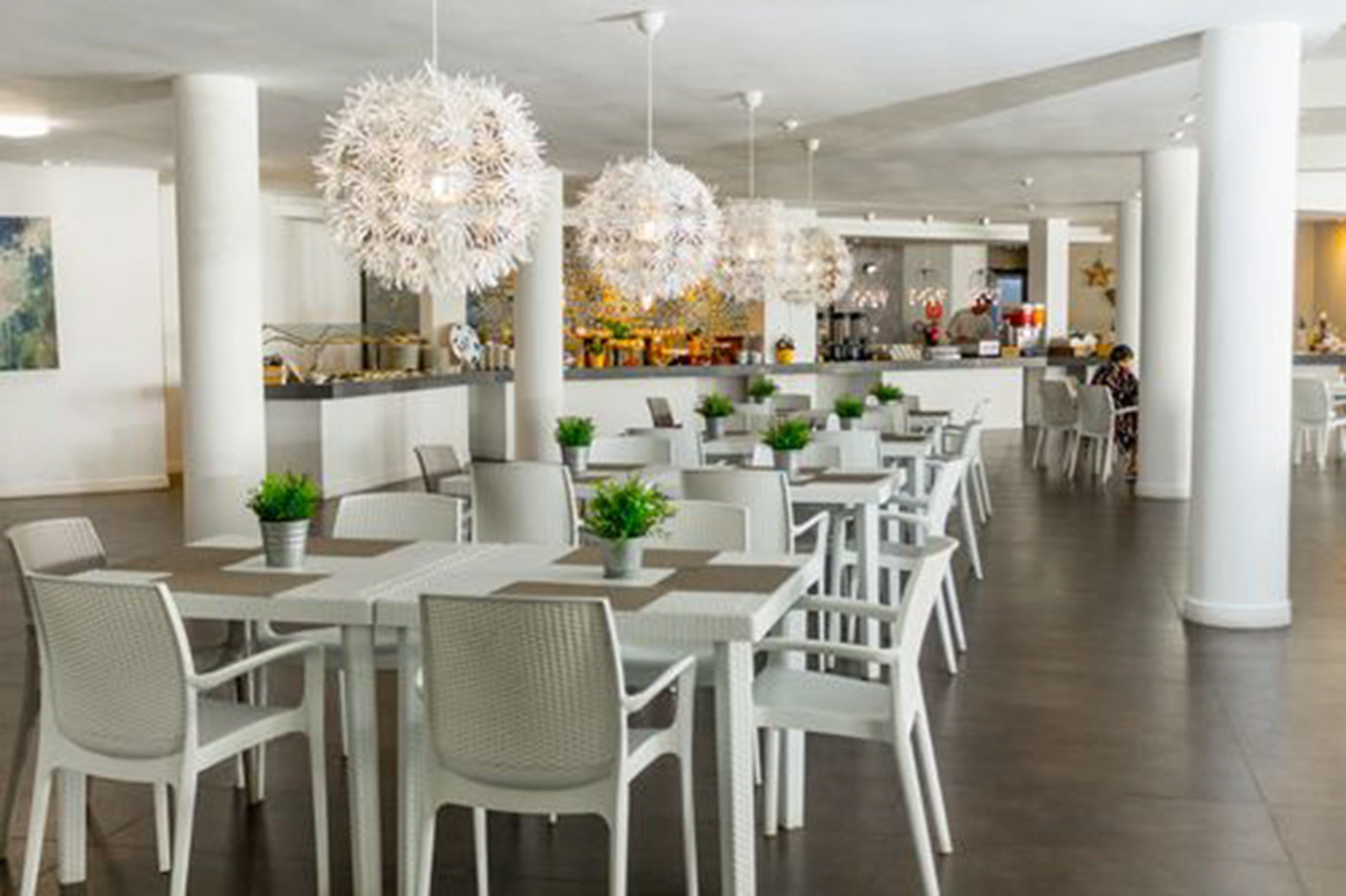 A modern dining area with white chairs and tables, large spherical hanging lights, and a central bar area.