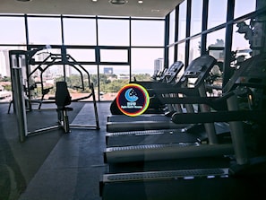 Un gimnasio con máquinas de cardio, equipo de levantamiento de pesas y amplias ventanas con vista a la ciudad.