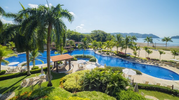 Ein Resort mit mehreren Pools, Palmen und Blick auf den Strand.