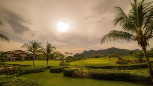 Ein Golfplatz mit gepflegten Rasenflächen, Palmen und einer Bergkulisse.