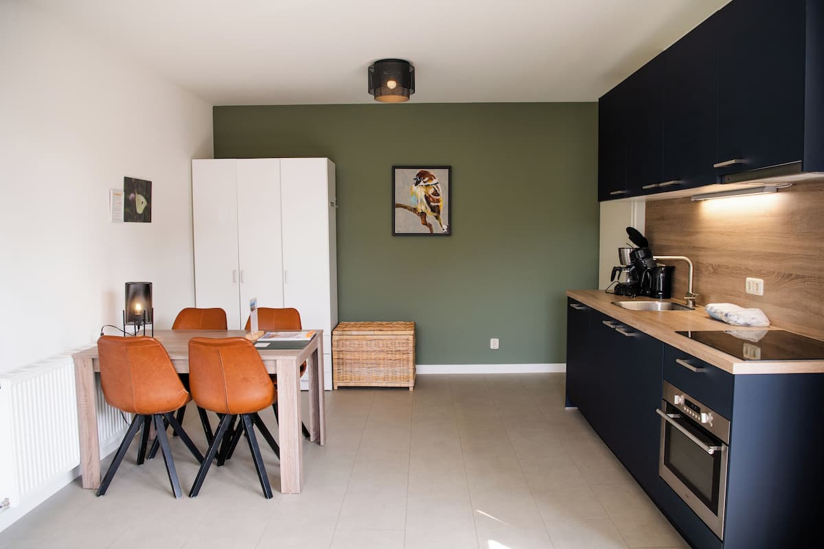 A modern kitchen with dark cabinets, a wooden countertop, and a dining area with chairs and a table.