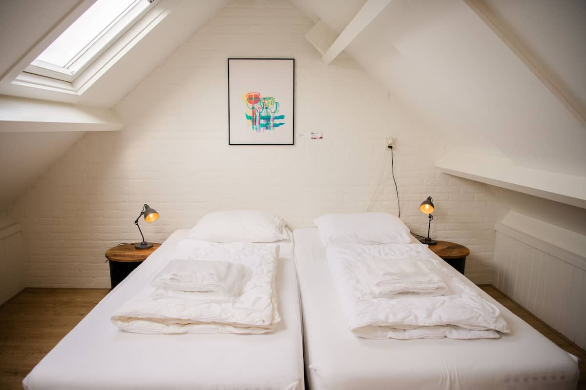 A bedroom with two beds, white bedding, a skylight, a framed artwork, and bedside lamps.