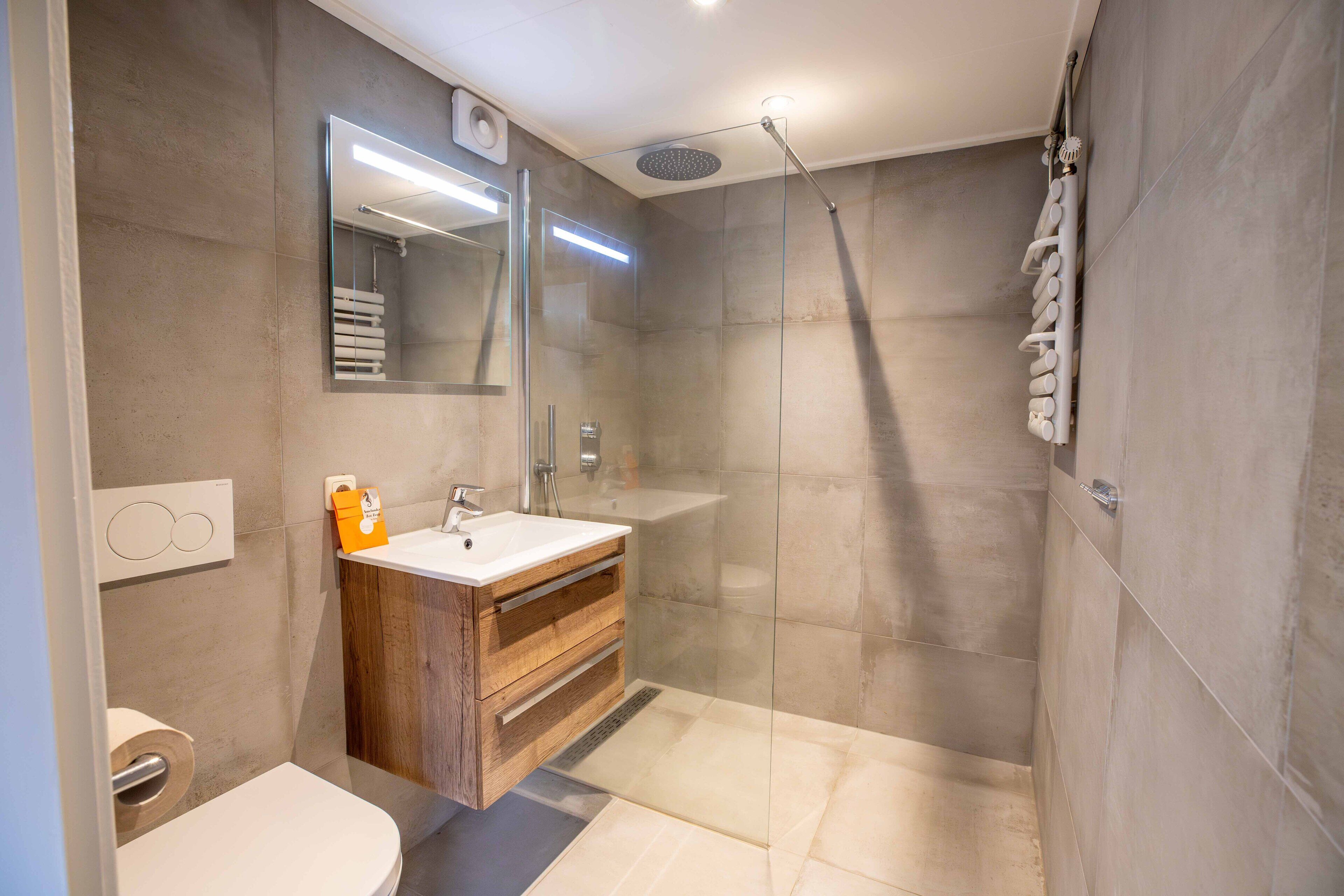 Une salle de bain moderne avec une douche à parois de verre, un meuble-lavabo en bois et un grand miroir.
