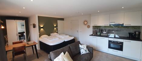 A modern hotel room with a bed, a sofa, a dining area, and a kitchenette.