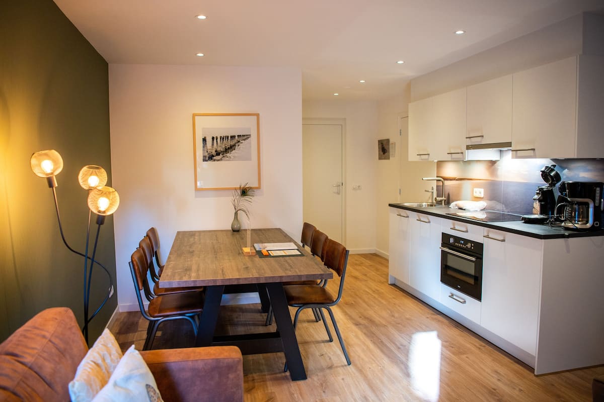 A modern kitchen with white cabinets, a wooden dining table, and a built-in oven.