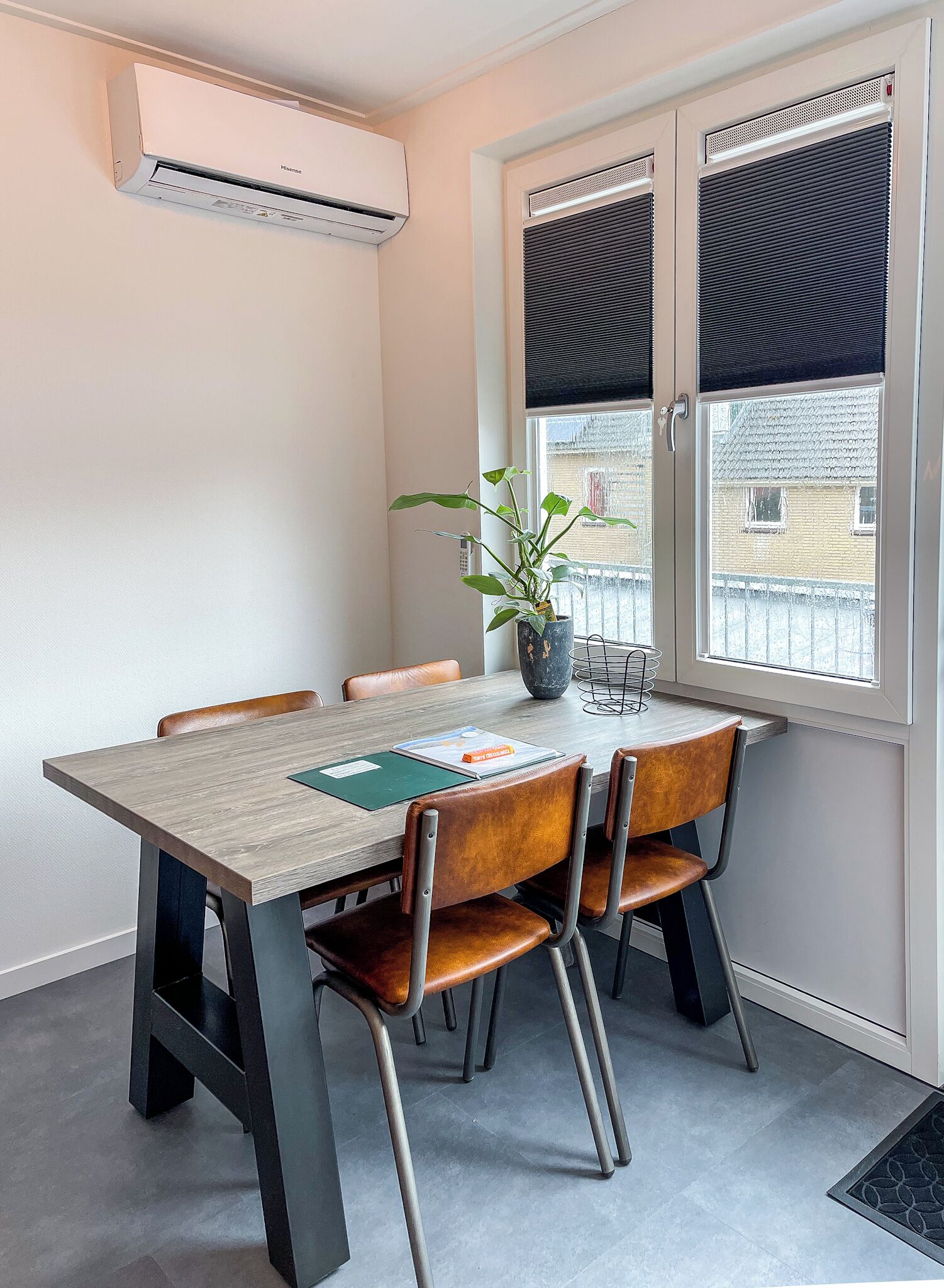 Un comedor con mesa, sillas, una planta en maceta y una ventana con persianas.