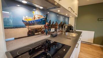 A modern kitchen with a central island, a built-in stove, and a backsplash depicting a maritime scene.