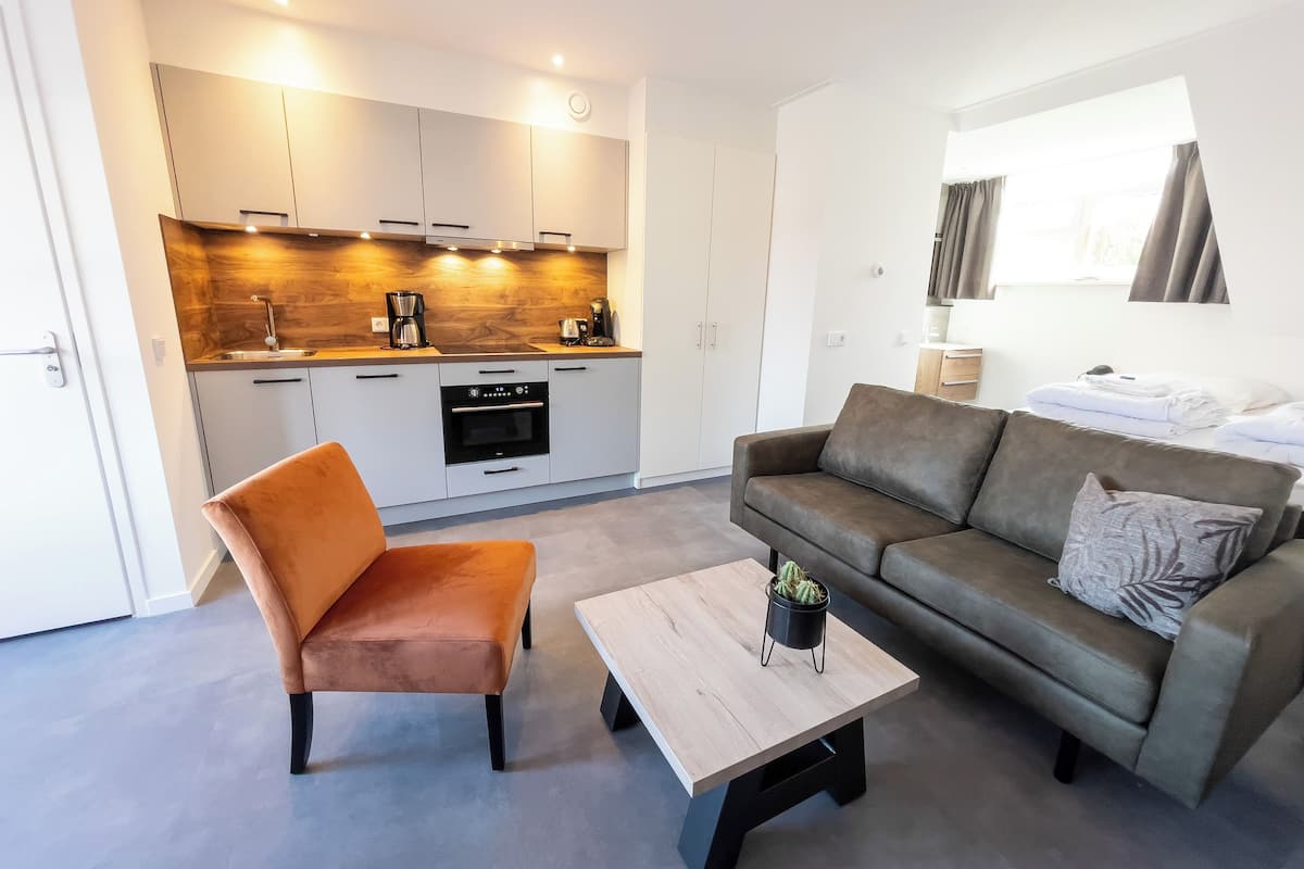 A modern kitchen with built-in appliances, a dining area with a sofa and coffee table, and a window with curtains.