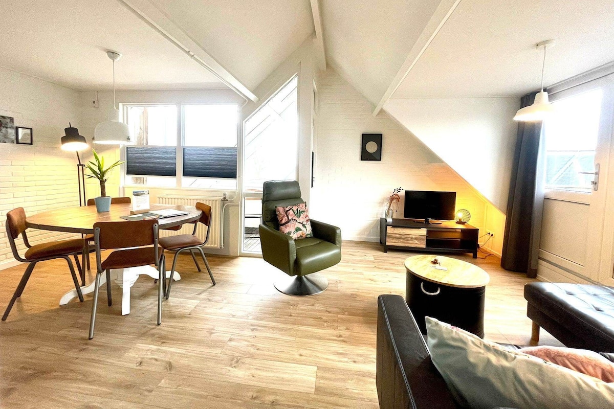A spacious loft apartment with a dining area, a green armchair, a sofa, and a TV.