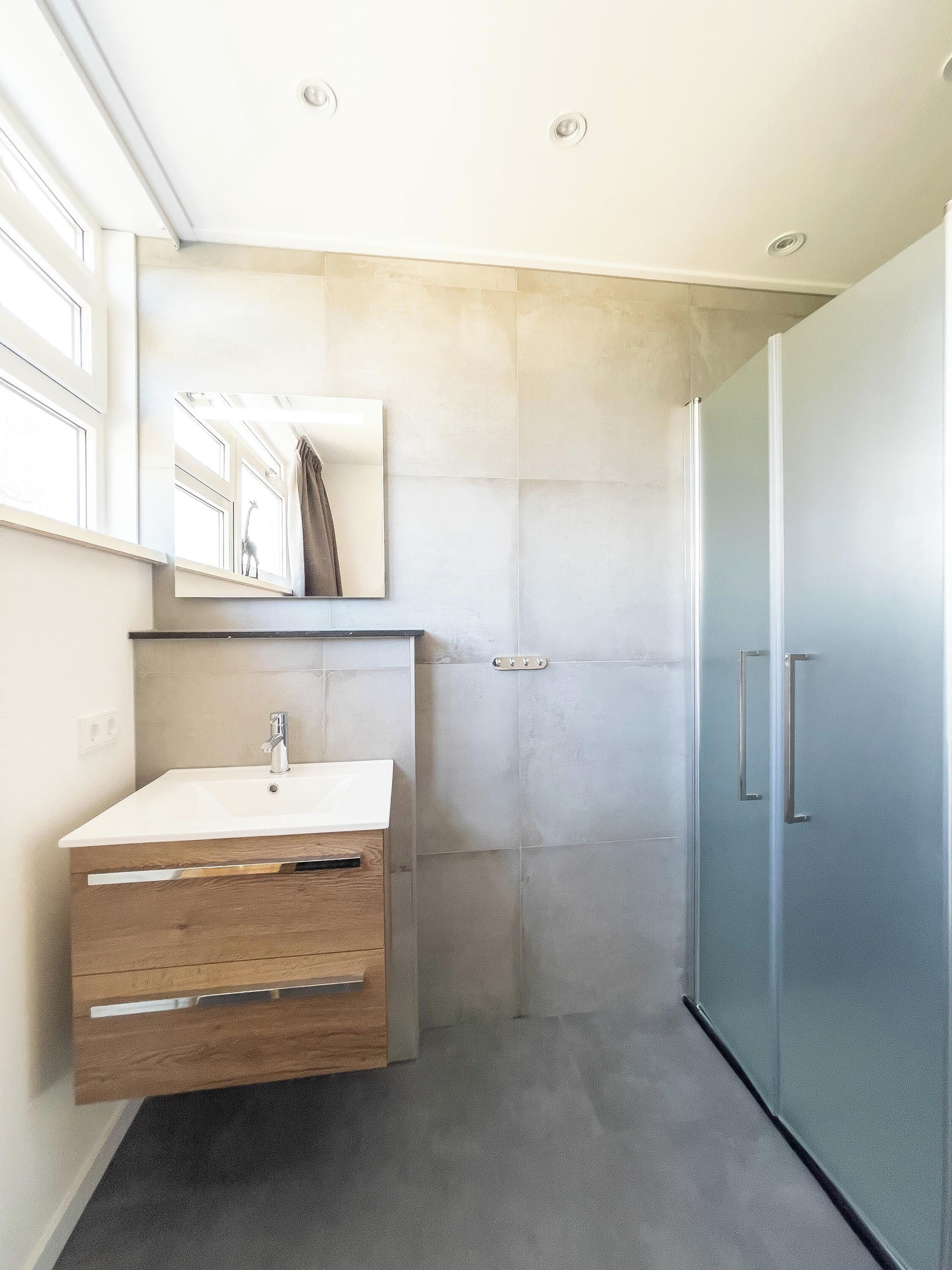 Un baño moderno con un lavabo blanco, un mueble de madera y una cabina de ducha de vidrio.