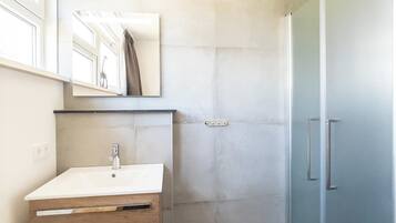 Un baño moderno con un lavabo blanco, un mueble de madera y una cabina de ducha de vidrio.