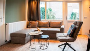 A modern living room with a sectional sofa, a round coffee table, and a high chair. - De Vlindertuin Ameland (Nes)