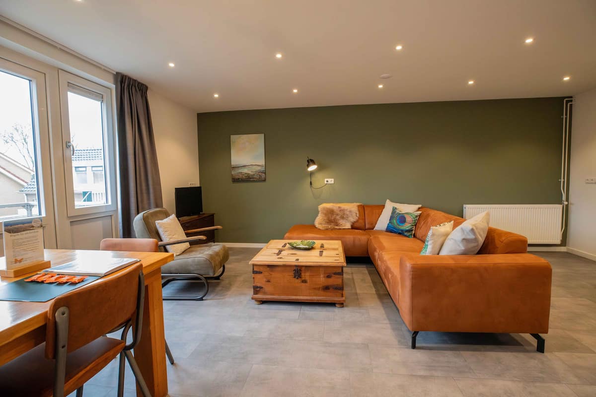 A modern living room with a sofa, a wooden coffee table, a dining table with chairs, and a painting on the wall.