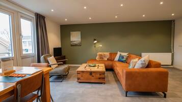 A modern living room with a sofa, a wooden coffee table, a dining table with chairs, and a painting on the wall.