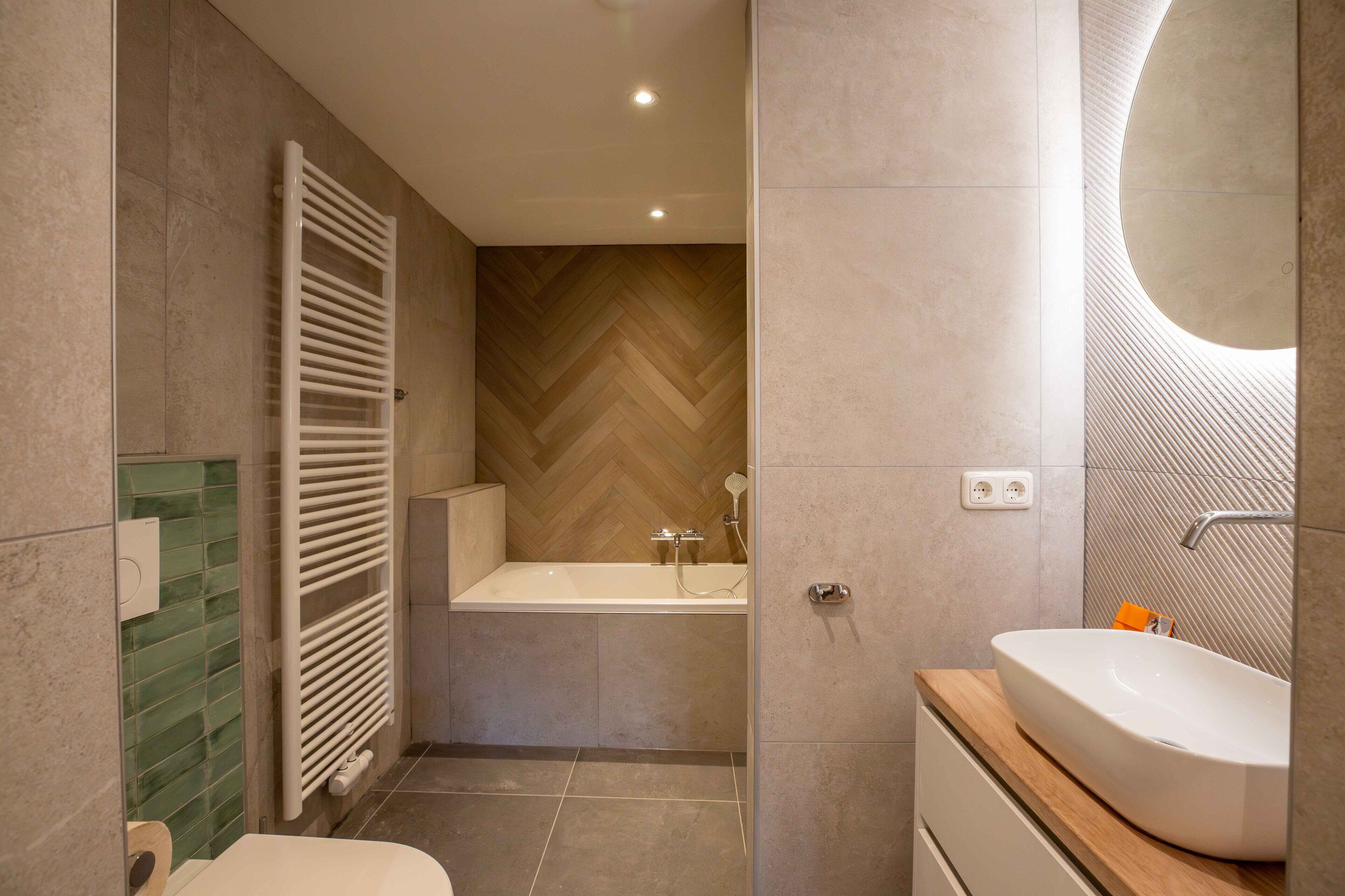 Ein modernes Badezimmer mit einer freistehenden Badewanne, einem großen Spiegel und einer Wand mit Holzvertäfelung in Fischgrätmuster.
