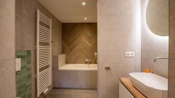 Ein modernes Badezimmer mit einer freistehenden Badewanne, einem großen Spiegel und einer Wand mit Holzvertäfelung in Fischgrätmuster.
