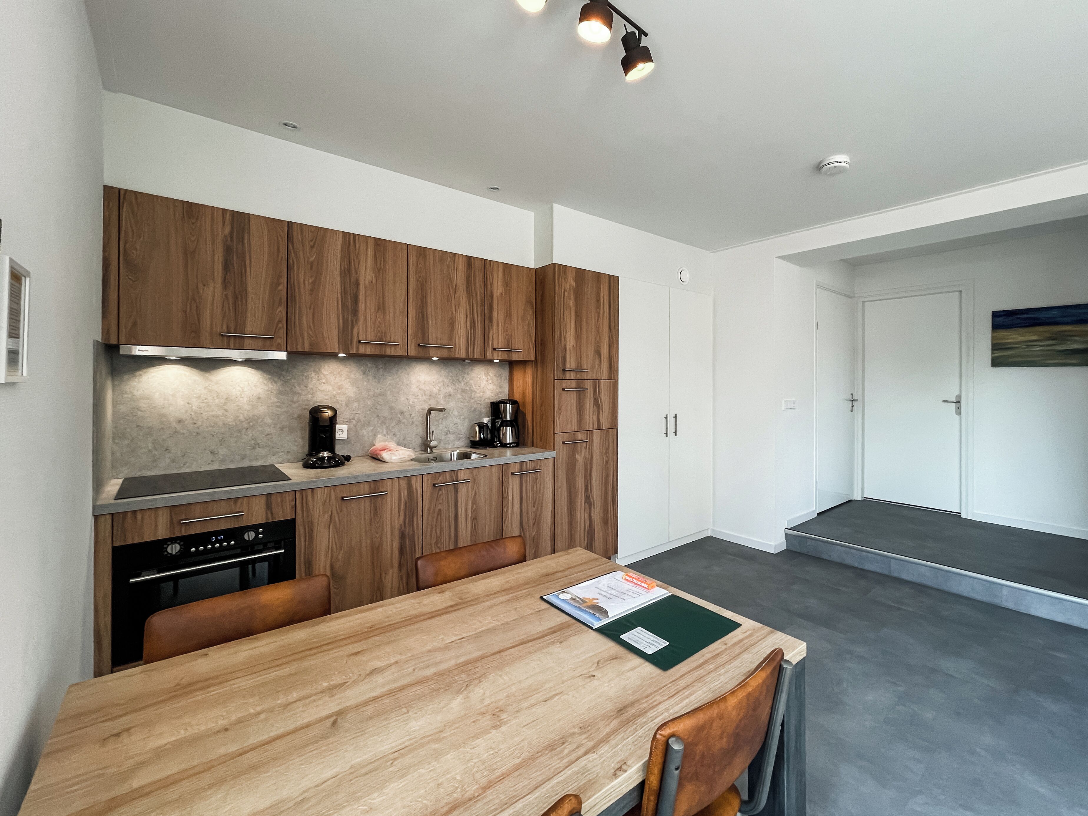 A modern kitchen with wooden cabinets, a stainless steel sink, and a dining area with a wooden table and chairs.