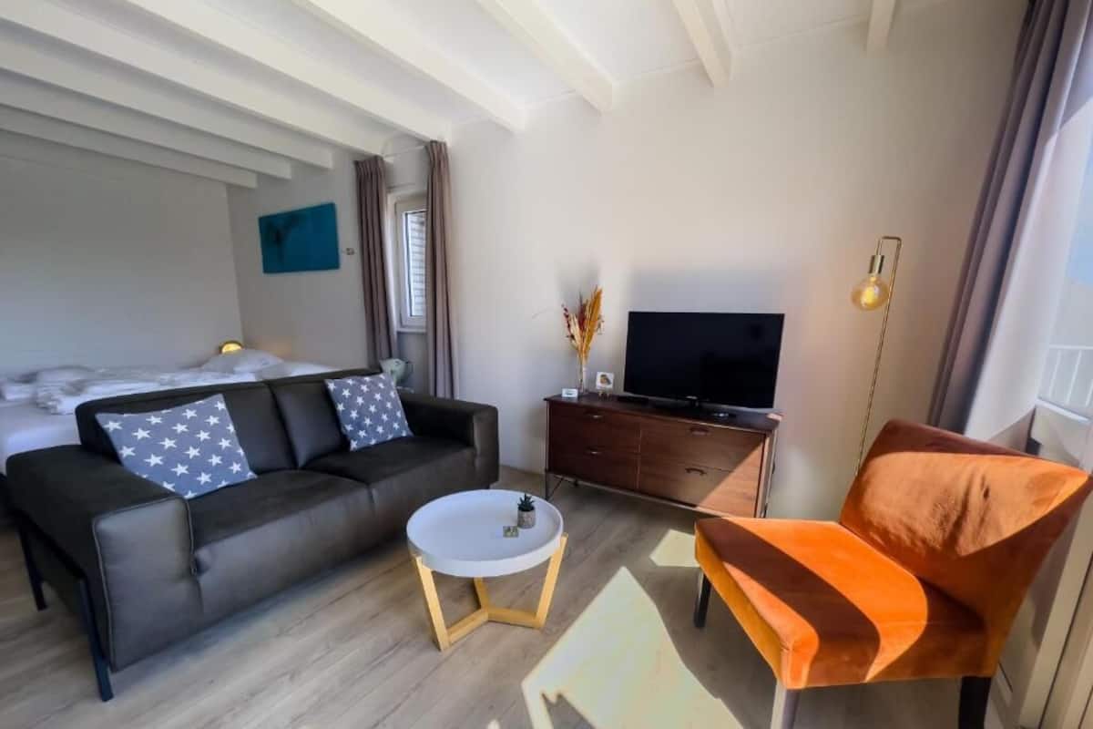 A modern living room with a sofa, a coffee table, a TV, and a unique orange chair.