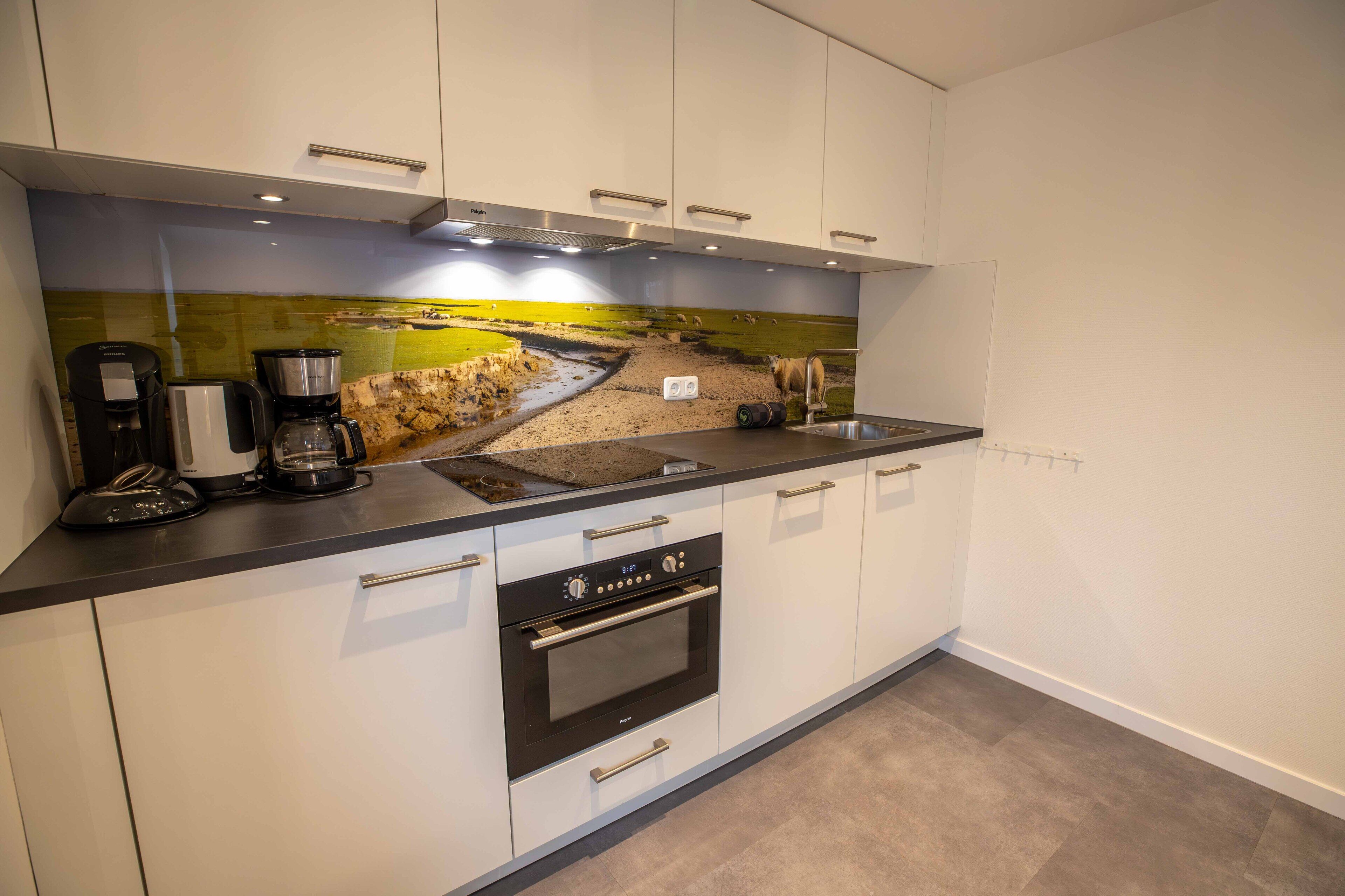 Een moderne keuken met witte kasten, een inbouwoven, een koffiezetapparaat en een spatwand met een landschapsontwerp.