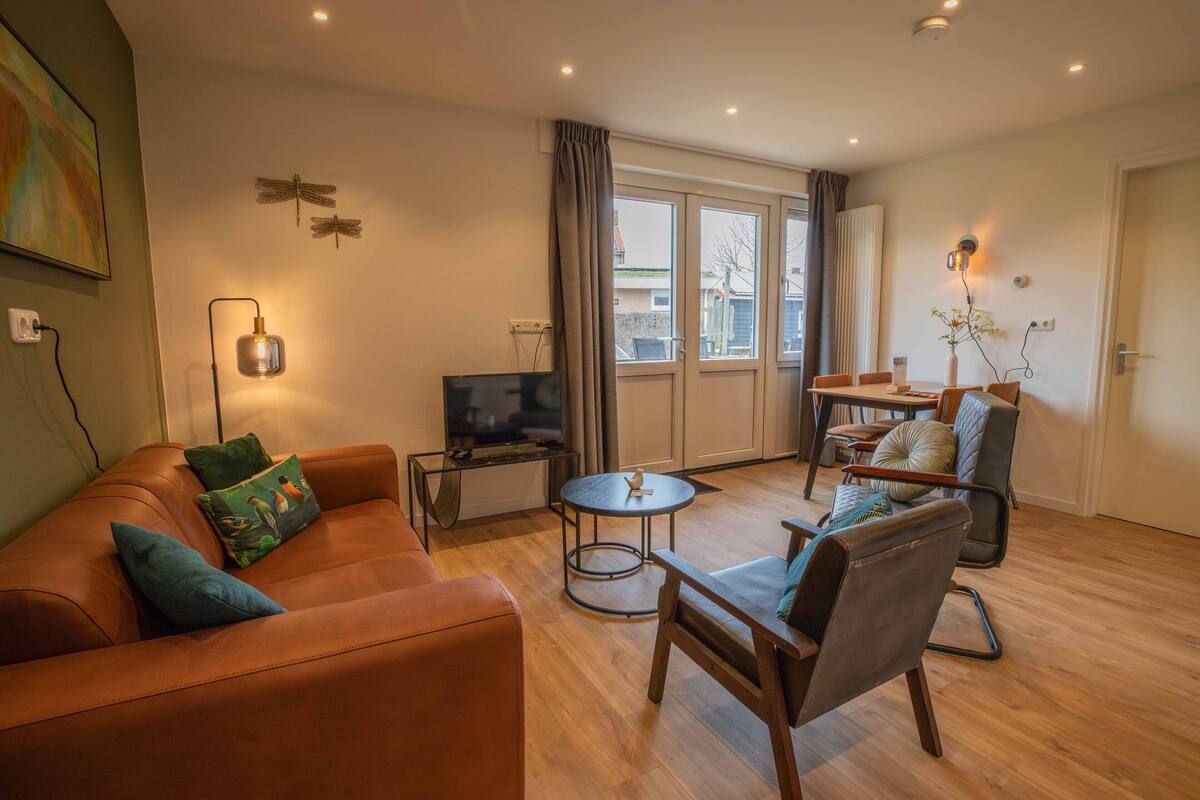 A modern living room with a leather sofa, a round coffee table, and a TV. There is a dining area with a table and chairs.