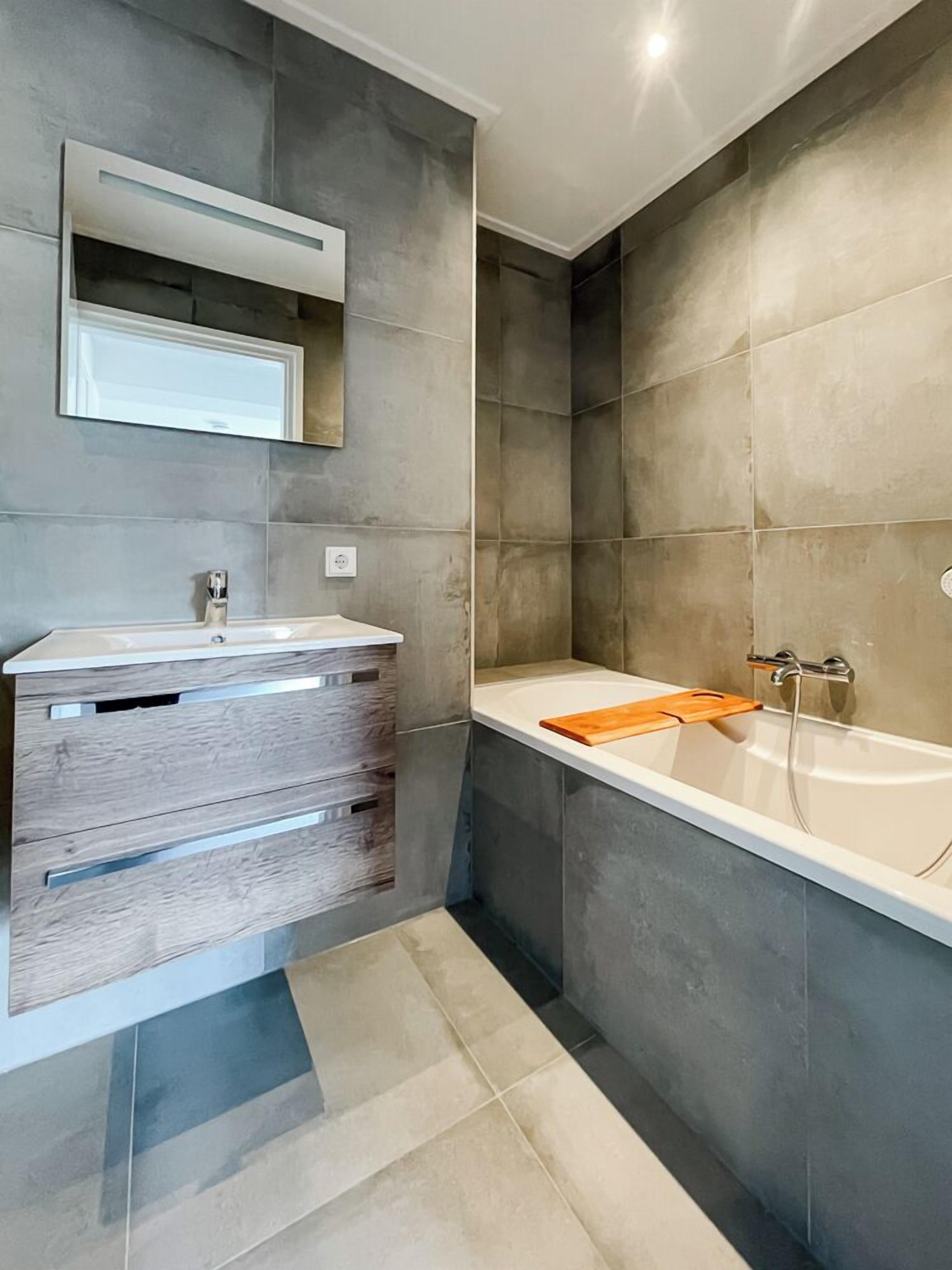 A modern bathroom with a white vanity, a large bathtub, and a mirror above the vanity.