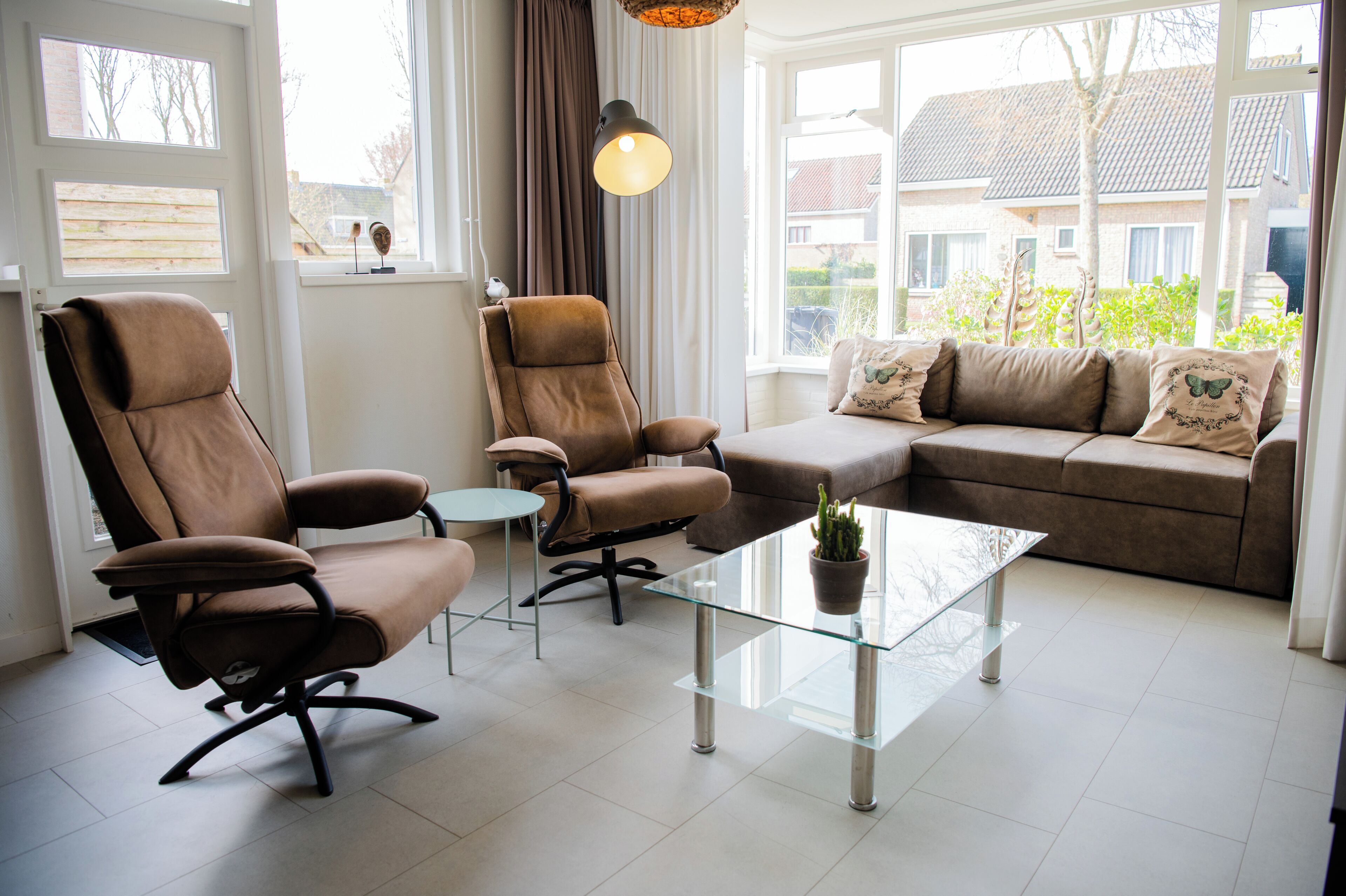 Una sala moderna con un sofá de cuero marrón, dos sillones de cuero marrón, una mesa de centro de vidrio y una planta en maceta.