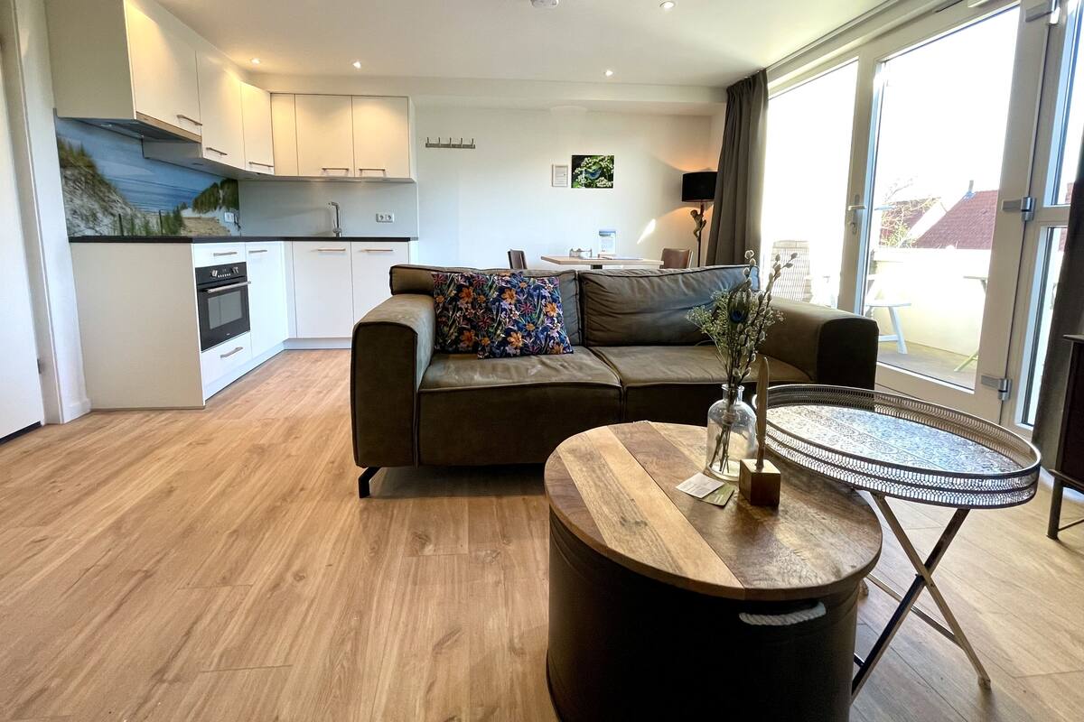 A modern living room with a sofa, a coffee table, and a kitchen in the background.