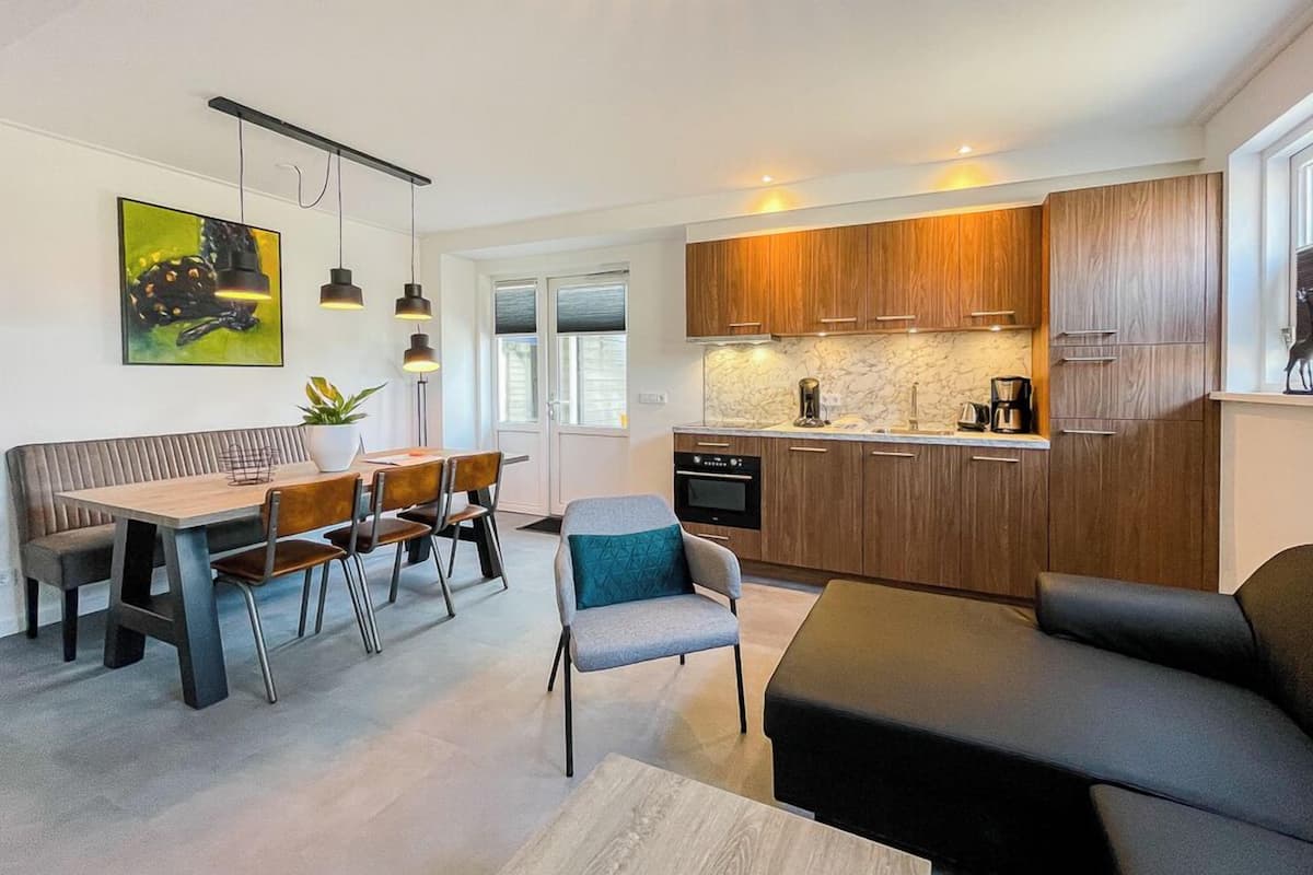A modern kitchen with wooden cabinets, a dining area with a bench and chairs, and a living area with a sofa.