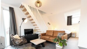 A modern living room with a staircase, a sofa, a coffee table, a TV, and a plant. - De Vlindertuin Ameland (Nes)