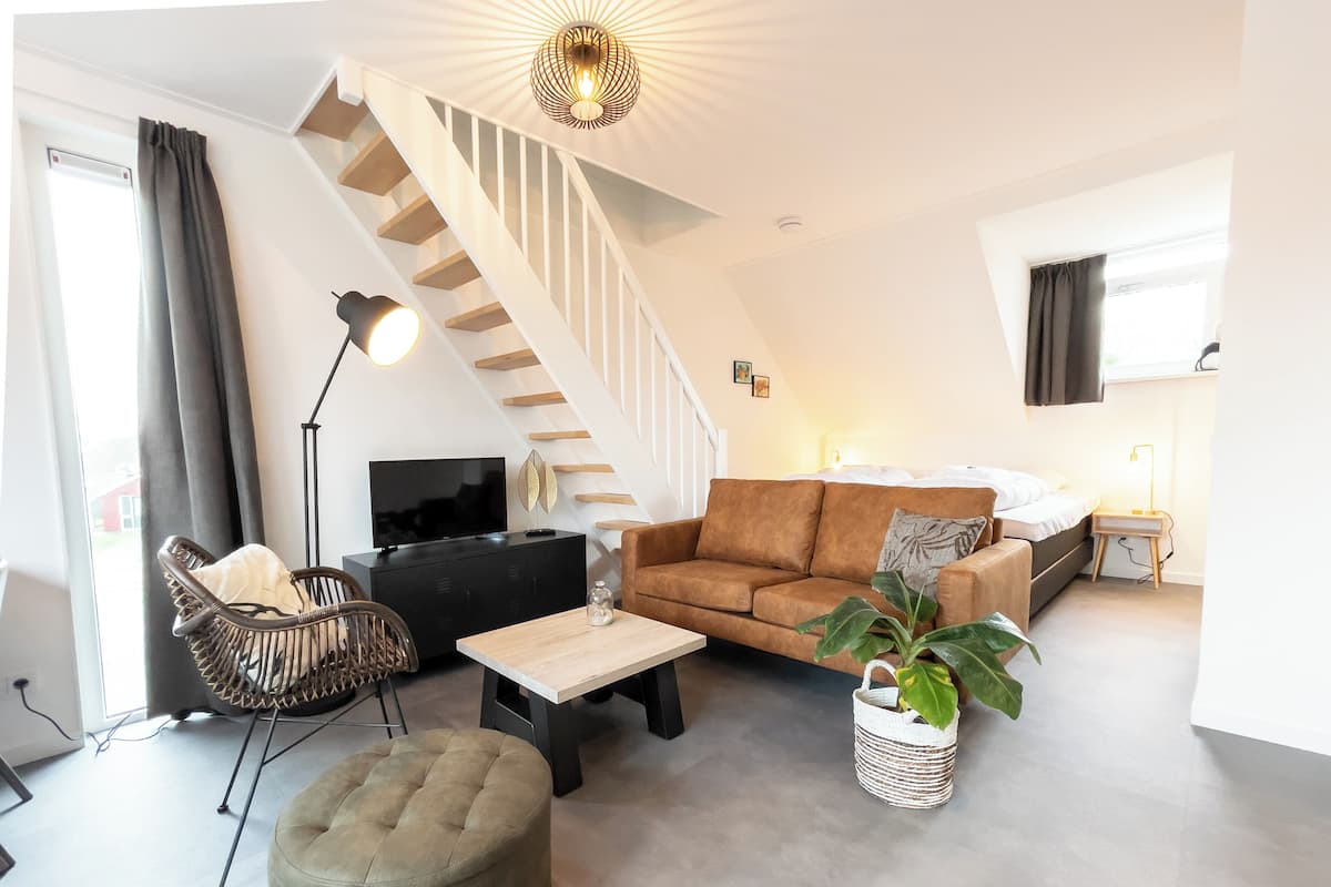 A modern living room with a staircase, a sofa, a coffee table, a TV, and a plant.