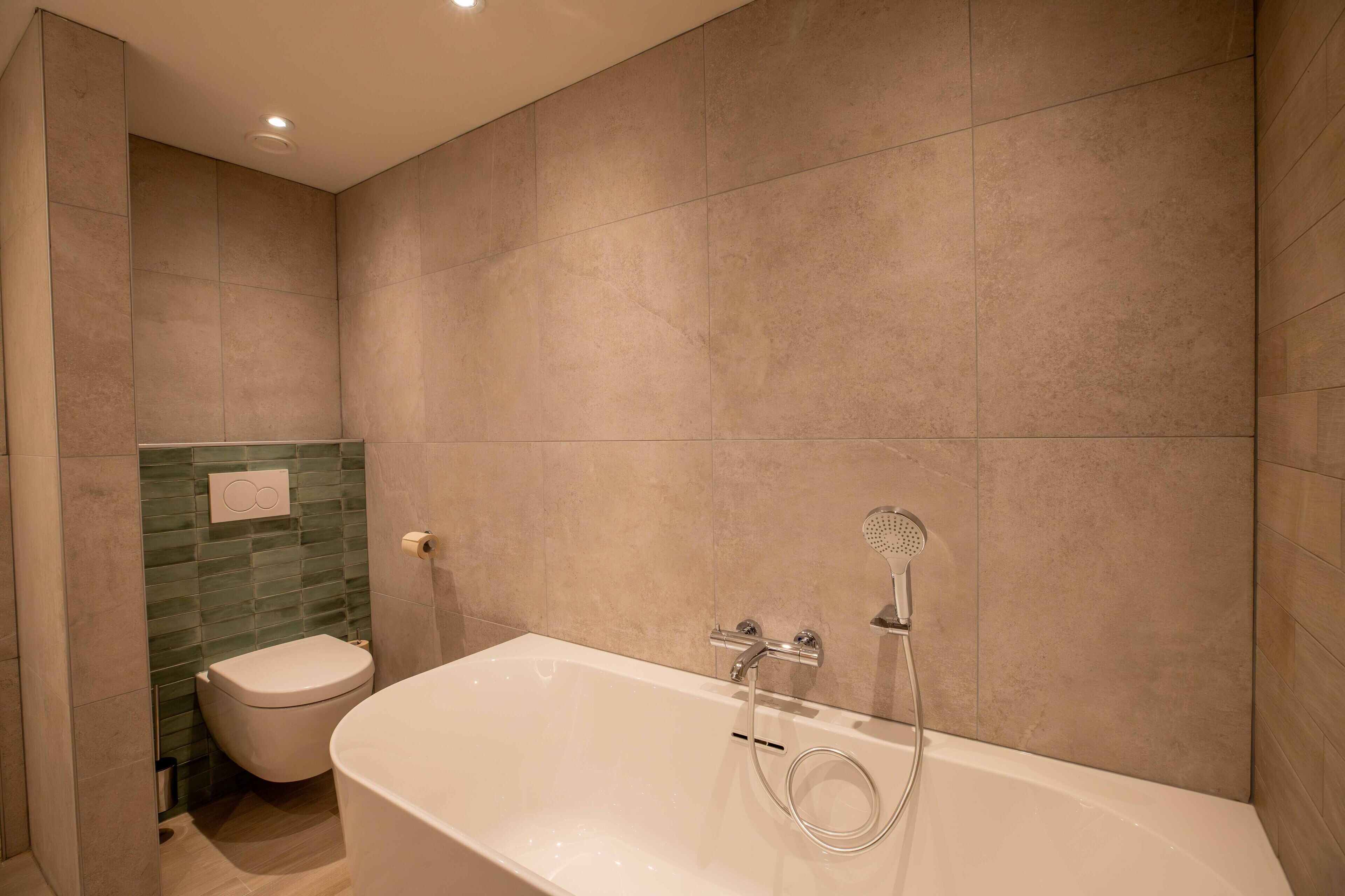Een moderne badkamer met een bad, toilet en douche.