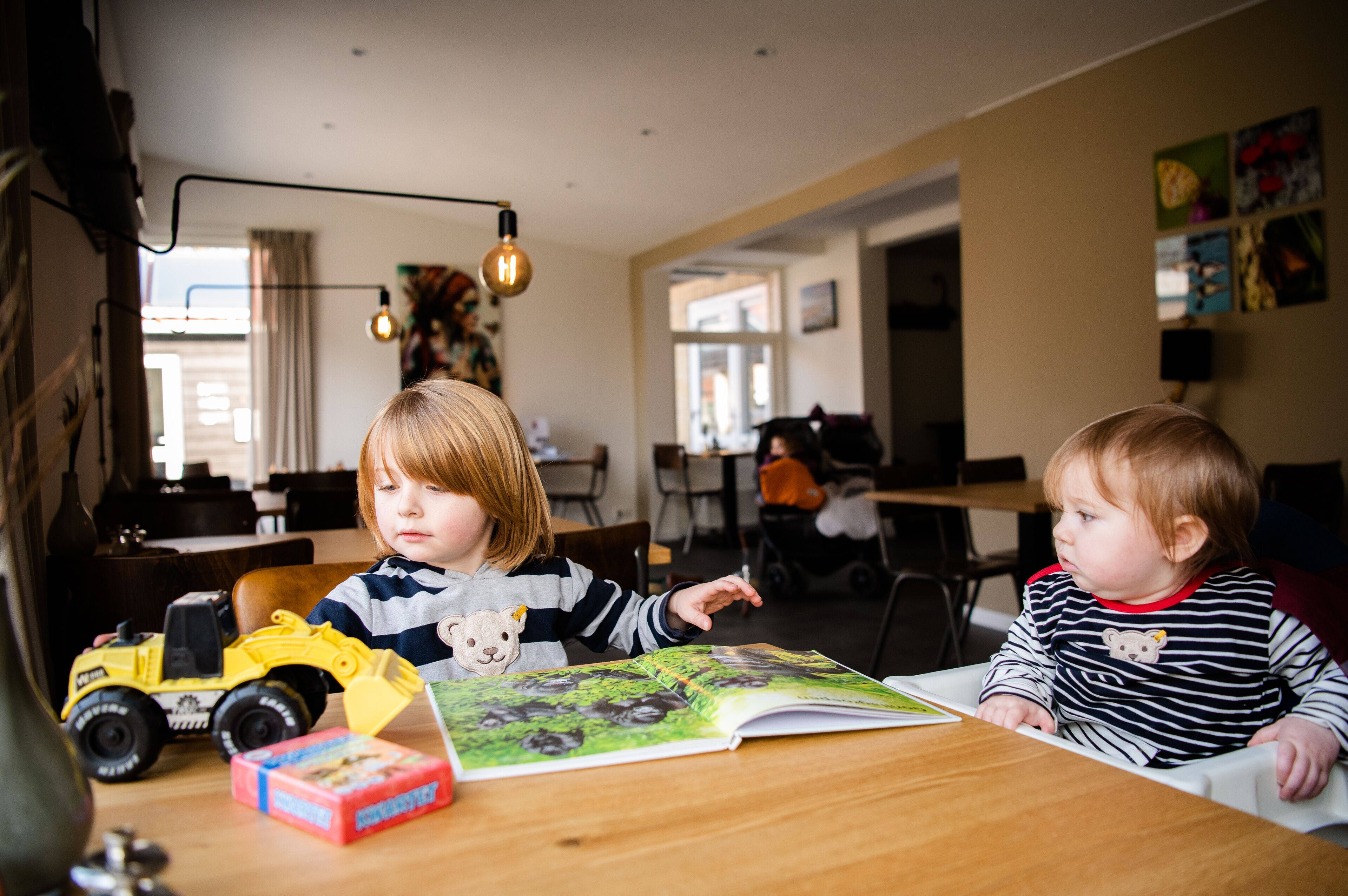 Two children at a wooden table with toys and a book.