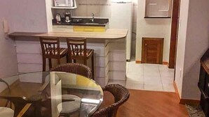 Une cuisine compacte équipée d’un four à micro-ondes, d’une cuisinière et d’un évier. Un coin repas est aménagé avec une table en verre et des chaises en osier.